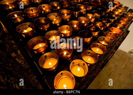 votive candles inside church rack of dozens of candles burning religious ceremony custom practice Stock Photo