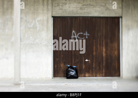 Garbage bag leaning against door graffitied with word 'act' Stock Photo