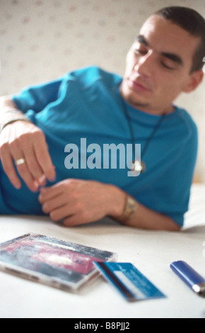 Young man reclining on bed smoking, line of cocaine on cd case in foreground Stock Photo