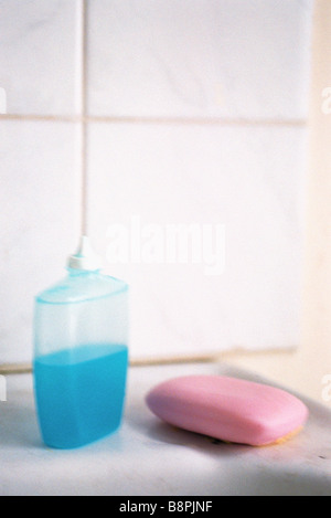 Bottle of blue liquid soap, pink bar of soap set on bathroom ledge Stock Photo