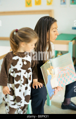 Teacher reading book aloud, child standing nearby Stock Photo