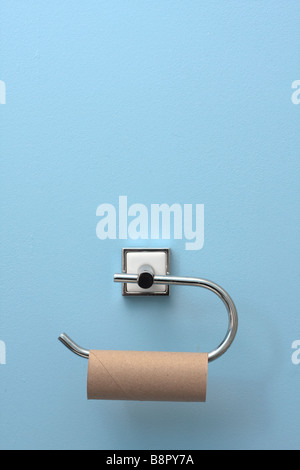 An empty toilet roll on a wall mounted toilet roll holder against a blue wall Stock Photo