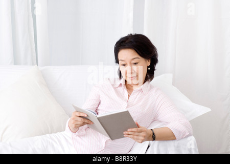 Senior woman reclining on sofa reading book portrait Stock Photo