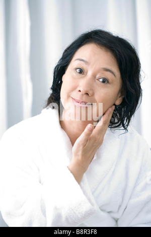 Senior woman in bathrobe touching face smiling portrait Stock Photo