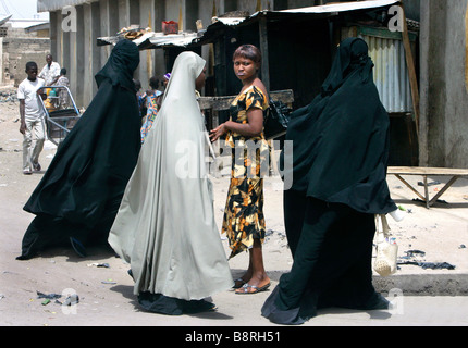 A sceptic looking modern dressed christian woman looking at muslim women wearing a full body burka. Maiduguri, Borno State, Nigeria Stock Photo