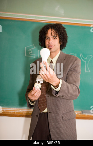 teacher in american classroom holding energy efficient compact fluorescent light bulb and traditional bulb, comparing energy use Stock Photo