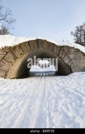 Ski track on frozen river passing under the arched bridge. Stock Photo