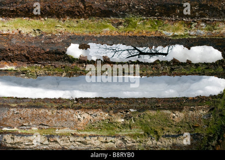 View through the hole in old metal bridge decking covered with snow on leafless tree branch. Stock Photo
