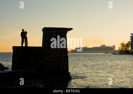 A young couple enjoys the sunrise on the dive tower at Coconut Island in Hilo Bay - Hilo, Big Island, Hawaii, USA Stock Photo