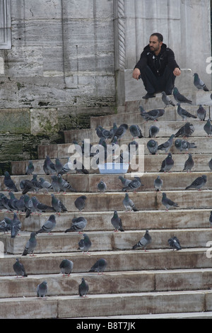 Man surrounded by pigeons waiting at the entrance of the New Mosque in Istanbul. Stock Photo