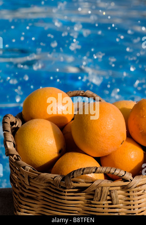 ORANGES BASKET POOLS SPLASH SUN FRESH SPAIN Basket of sunny Spanish oranges with swimming pool and splashing water behind Stock Photo
