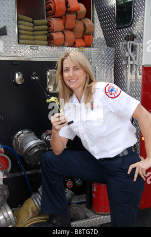 Smiling Female firefighter paramedic EMT in dress uniform talking on two way radio in front of fire engine Stock Photo