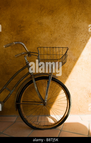 Old bicycle leans against a rustic wall in the shade Stock Photo