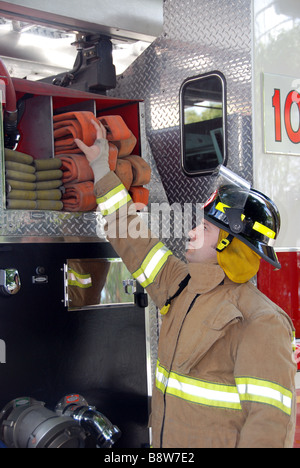 Male Firefighter reaching for fire hose on fire truck wearing bunker gear and helmet Stock Photo