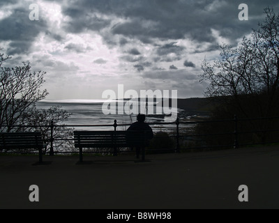 A man sits in a winter scene overlooking the harbour at Scarborough, United Kingdom. Stock Photo