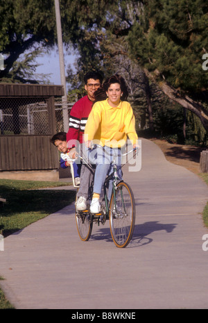 Hispanic mom mother dad father child ride tandem bike bicycle outdoor outside park happy fun smile laugh enjoy share Stock Photo