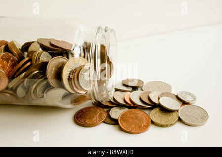 UK sterling coins spilling out of a glass jam jar Stock Photo