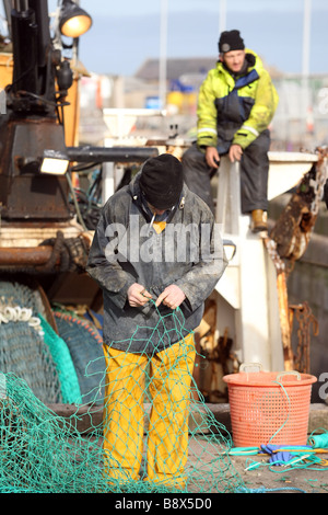 North Sea fishermen mending and repairing fishing nets in the harbour at Peterhead, Aberdeenshire, Scotland, UK Stock Photo