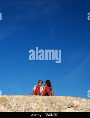 Couple sitting on a wall in red trousers in Alghero, Sardinia Stock Photo