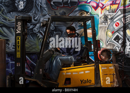 Graffiti Five Points neighborhood Queens New York man driving forklift on loading dock with bandanna covering his mouth and nose Stock Photo