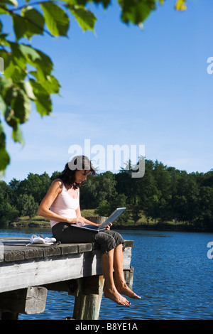A woman with a laptop on a jetty by a lake Sweden. Stock Photo