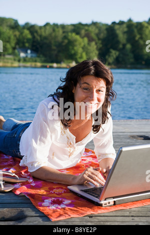 A woman with a laptop on a jetty by a lake Sweden. Stock Photo