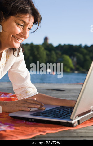 A woman with a laptop on a jetty by a lake Sweden. Stock Photo