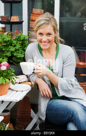 A blond woman drinking coffee in a greenhouse Sweden. Stock Photo