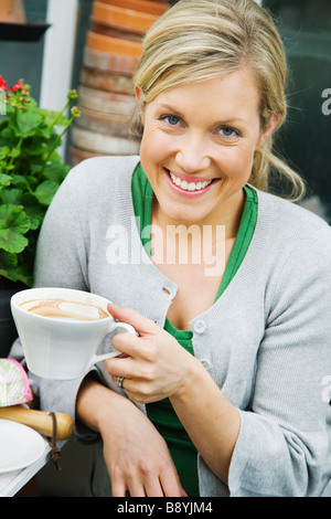 A blond woman drinking coffee in a greenhouse Sweden. Stock Photo