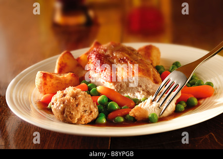 Traditional roast chicken dinner with roast potatoes and stuffing, served on a plate on a wood table Stock Photo