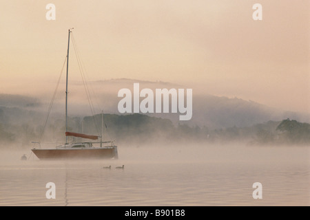 Misty view of boat on Lake Windermere at dawn from Cockshott Point Cumbria Stock Photo