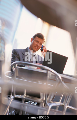 Young businessman at cafe wiith laptop talking on cell phone Stock Photo