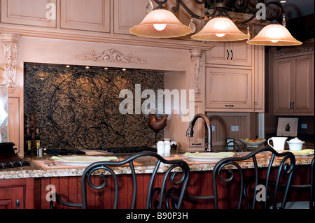 A designer kitchen with granite counters stainless appliances a massive island with breakfast counter and a tile backsplash Stock Photo