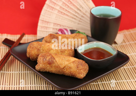 Crispy fried egg rolls with dipping sauce served on a bamboo mat with tea  Stock Photo