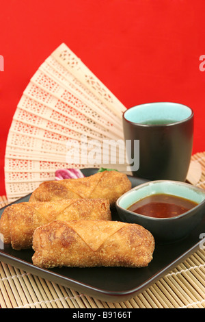 Crispy golden egg rolls served with tea against a red background Vertical with room for text  Stock Photo