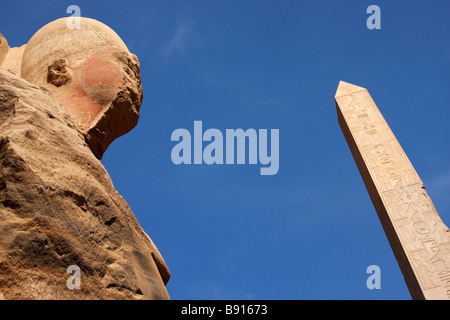 Head of colossal stone carved osiris statue and Obelisk of Queen Hatshepsut against blue sky, Temple of Karnak, Luxor, Egypt Stock Photo