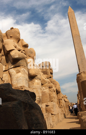 Row of large stone carved osiris statues beneath Obelisk of Queen Hatshepsut, Karnak Temple, Luxor, Egypt Stock Photo