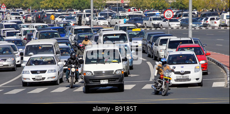 Dubai close up busy wide road junction cars & motorbikes in traffic moving off at lights surface car park beyond United Arab Emirates UAE Middle East Stock Photo