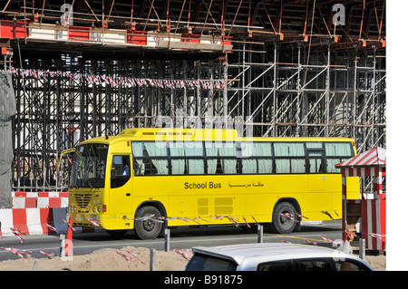 Dubai yellow school bus passing through scaffolding around bridge construction project for new Metro overhead transport system United Arab Emirates Stock Photo