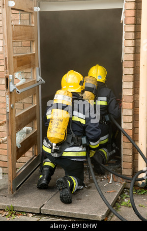 Two firefighters enter burning building wearing Breathing Apparatus BA Stock Photo