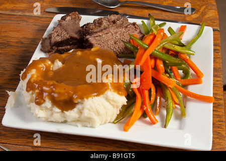 Mashed potatoes, gravy, pot roast with julienned green beans and carrots on a white plate Stock Photo