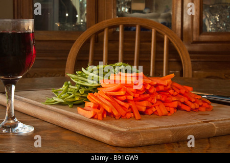 A cutting board with jullienned carrots and green beans with a knife and a glass of wine for the chef Stock Photo