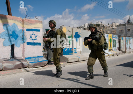 Israeli soldiers patrolling along concrete slabs separating Palestinian neighborhood of Bab a-Zawiya and H-2 Israeli control area in Hebron West Bank Stock Photo