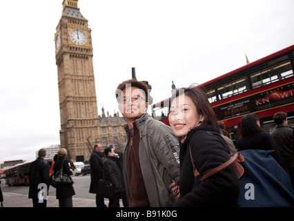 Asian oriental tourist couple in 20s / 30s visiting London, on street in front of Big Ben and London double decker red bus Stock Photo