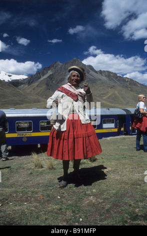 Old lady spinning wool using spindle  in front of Orient Express owned Puno to Cusco train at Abra La Raya pass, Peru Stock Photo