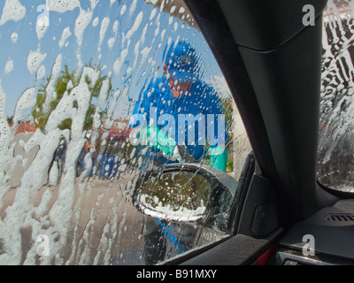 Man blurred by soap patterns on the driver's side window in a car wash a view from inside the car during the car wash Stock Photo