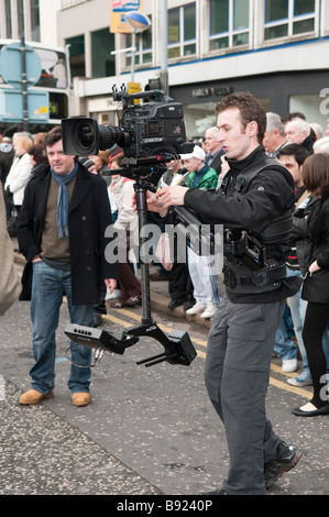 Cameraman operates a Steadycam in a crowd for an outside broadcast news report. Stock Photo