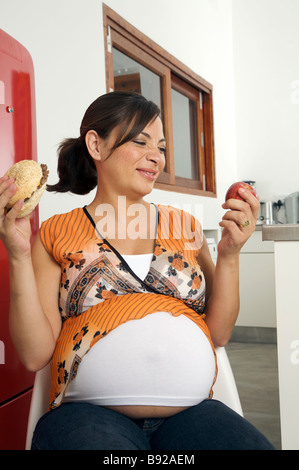 Pregnant woman choosing between apple or hamburger to eat Cape town Western Cape Province South Africa Stock Photo