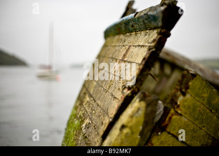 Wrecked hull of an old fishing boat with modern yacht in the background. Taken on the bank of the Camel river outside Padstow. Stock Photo