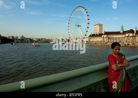 The London Eye on the Thames as seen from Westminster Bridge an Indain woman stands by Stock Photo